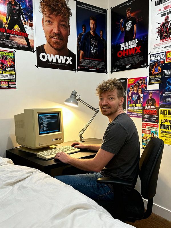 A person is sitting at a desk with a vintage computer, surrounded by movie posters.