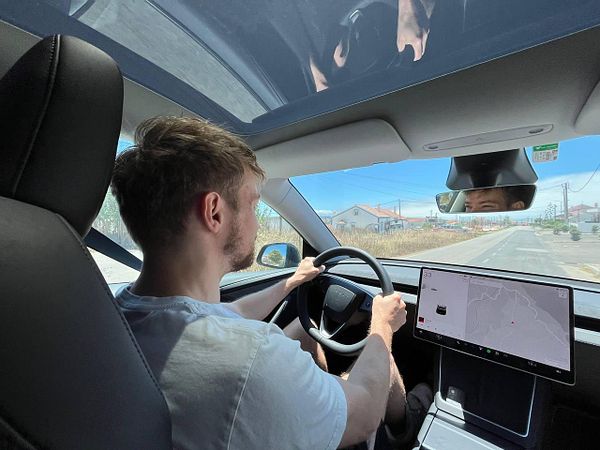 A person is driving a car on a sunny road with a digital display in front.