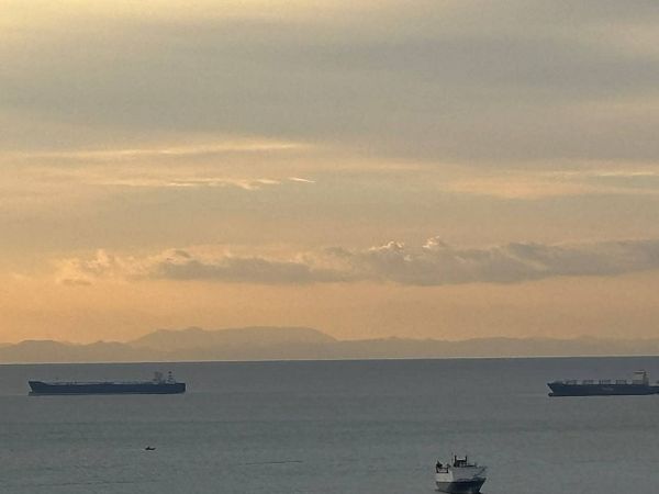 A distant view of Tsushima Island in Japan from Busan, Korea at sunset, featuring calm sea with three boats and a sky with soft clouds.
