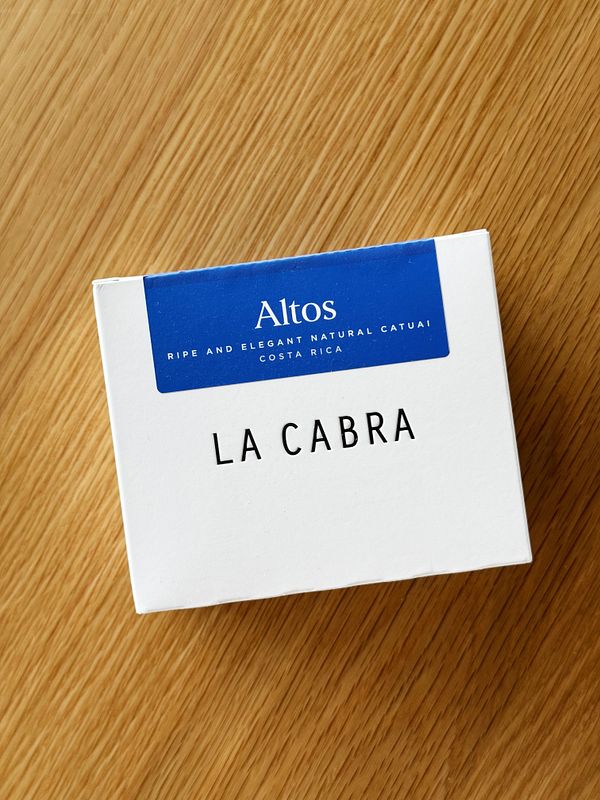 A coffee box labeled 'LA CABRA' is placed on a wooden surface.
