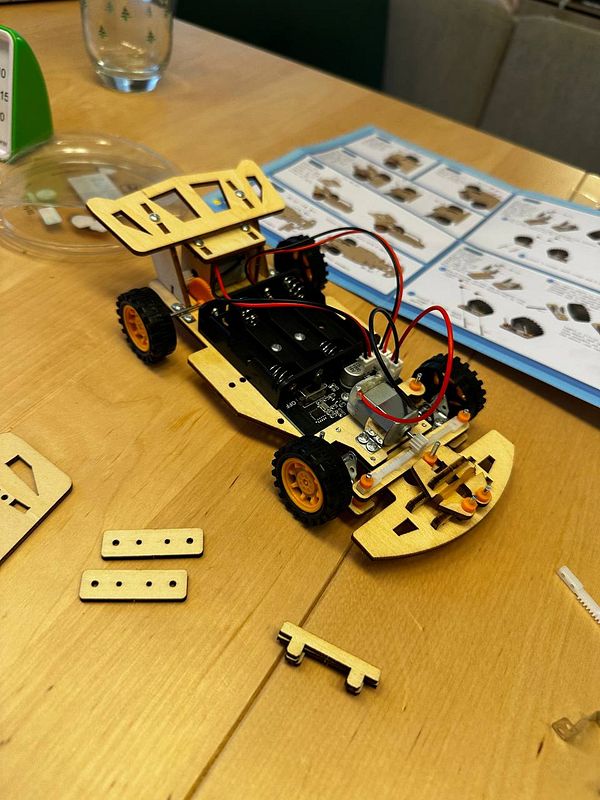 A partially assembled wooden toy car is displayed on a table with various components and instructions nearby.