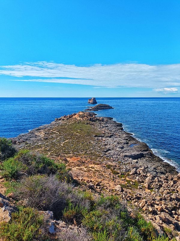 A scenic coastal view featuring a rocky peninsula extending into the ocean with a small island in the distance.