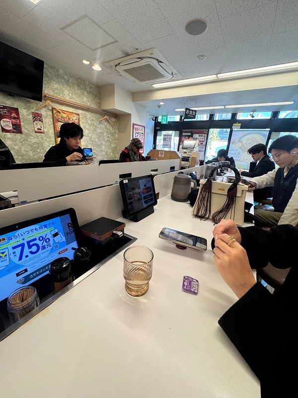A bustling Yoshinoya restaurant interior with patrons enjoying their meals and using digital ordering systems.