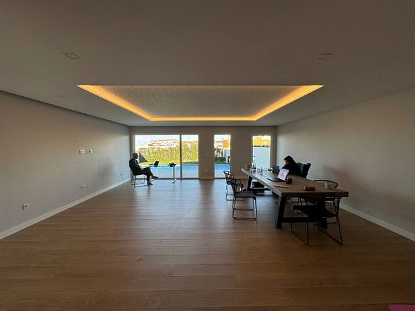 A spacious coworking area with two individuals working at a large table and a view of the outdoors.