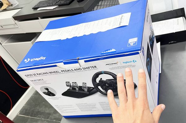 The image depicts a disassembled steering wheel controller with its internal components exposed, placed on a work surface with other gaming peripherals nearby.