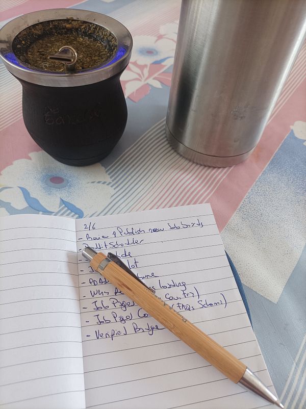 A workspace scene featuring a traditional mate cup, a stainless steel thermos, and a notebook with a to-do list.