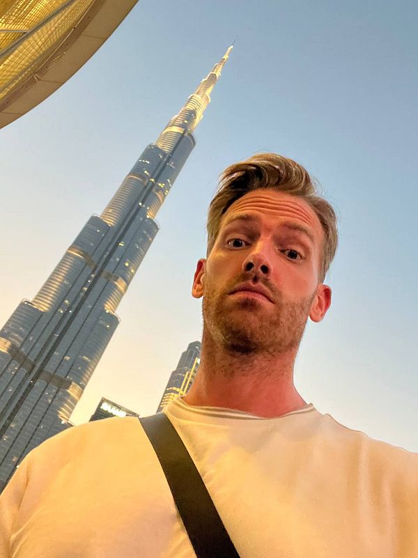 A man takes a selfie in front of the Burj Khalifa in Dubai during sunset.
