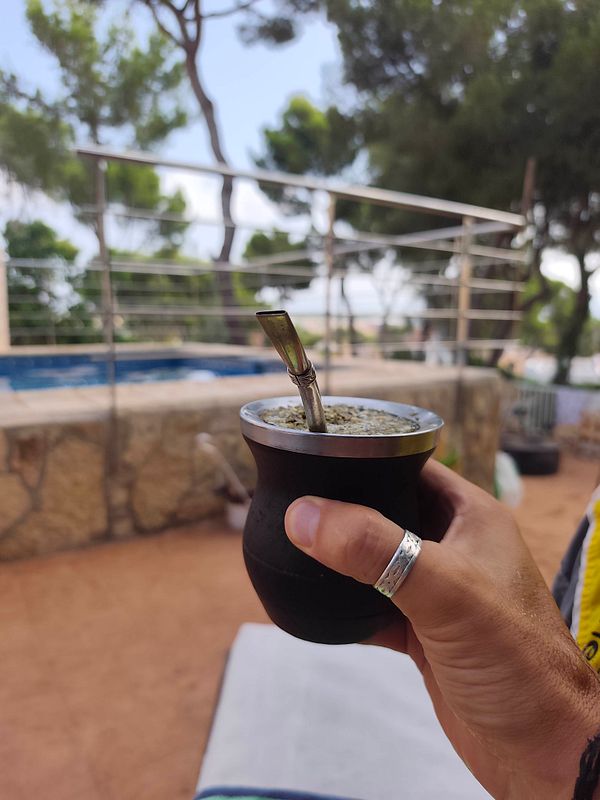 A person relaxing on a towel by a swimming pool, holding a drink, with a mate cup visible.