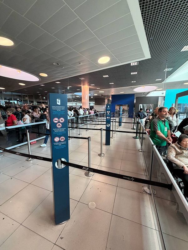 A crowded airport arrivals area with long queues cordoned by barriers and multiple signs overhead showing directions for EU and Non-EU arrivals.