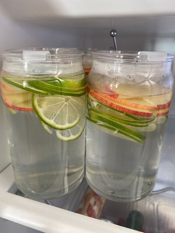Two jars of infused water with fresh fruits and herbs are placed in a refrigerator.