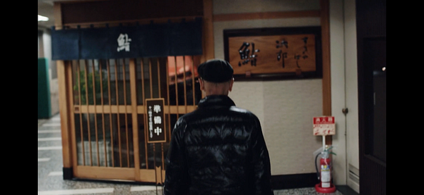 A person approaches a traditional sushi restaurant entrance in a dimly lit corridor.