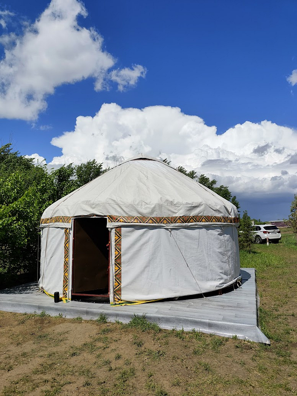 A traditional yurt is set against a bright blue sky with fluffy clouds.