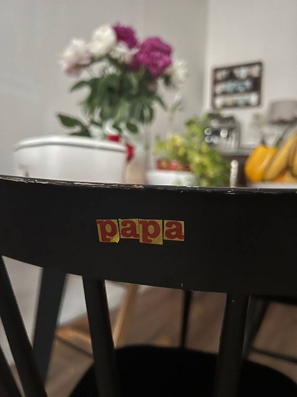 A black chair with the word 'papa' displayed on its backrest, set against a blurred background of a cozy room.