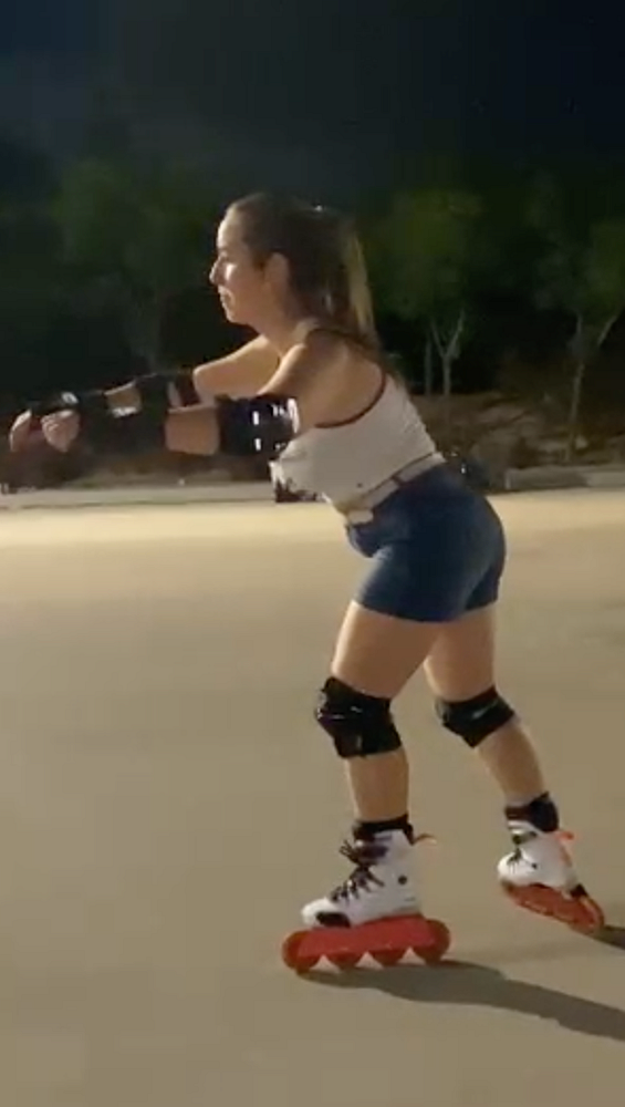 A woman is rollerblading at night while wearing protective gear.
