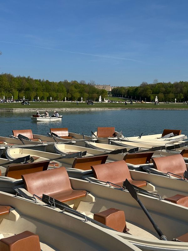 A scenic view of rowboats on a tranquil lake in Versailles, with lush greenery and the palace in the background.