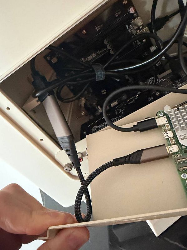 Open retro PC case with internal circuit board and attached Raspberry Pi 5 being inspected with cables connected.