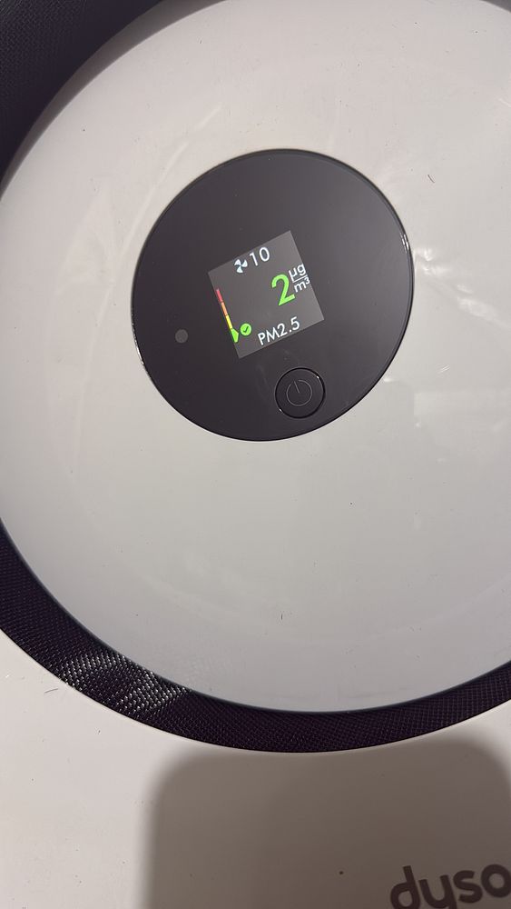 The image displays a digital air quality monitor showing PM2.5 levels in an office room.