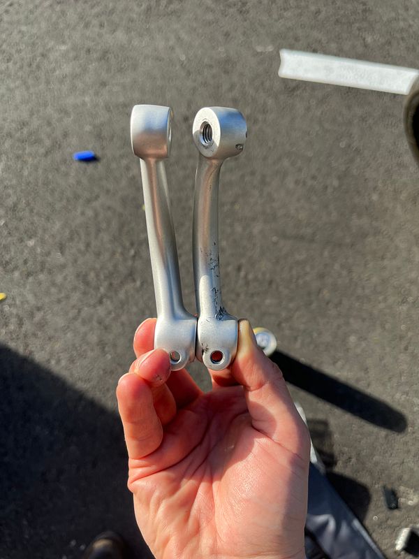 A hand holds two shifter levers, one bent and one straight, against a pavement background.