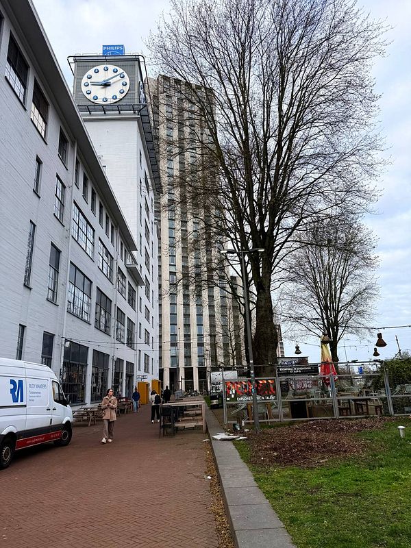 Interior view of a modern coworking space with rows of desks, chairs, and large windows with blinds in Eindhoven.