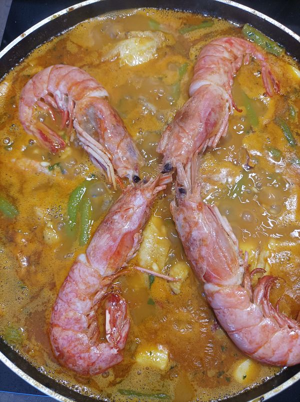 A close-up view of a paella dish featuring large shrimp and various ingredients simmering in a pan.