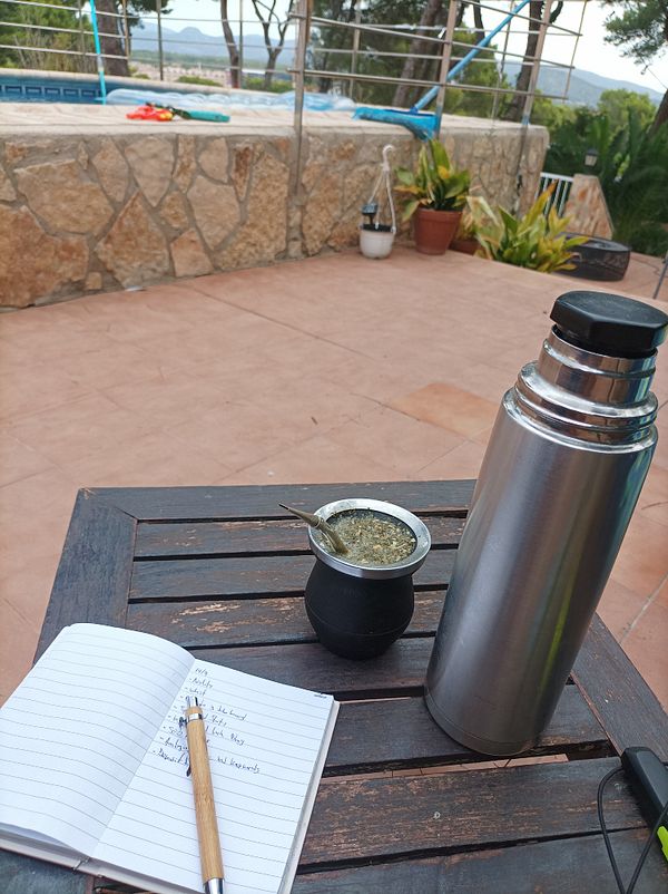 A serene outdoor workspace featuring a notebook, a mate cup, and a thermos.