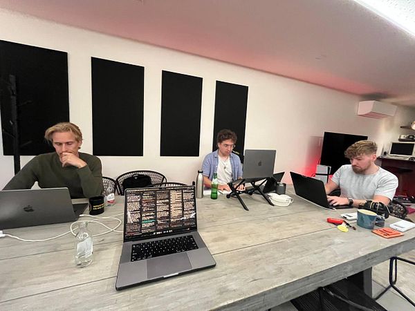 Illustration featuring five diverse people interacting in a shared workspace with multiple desks, computers, and office items.