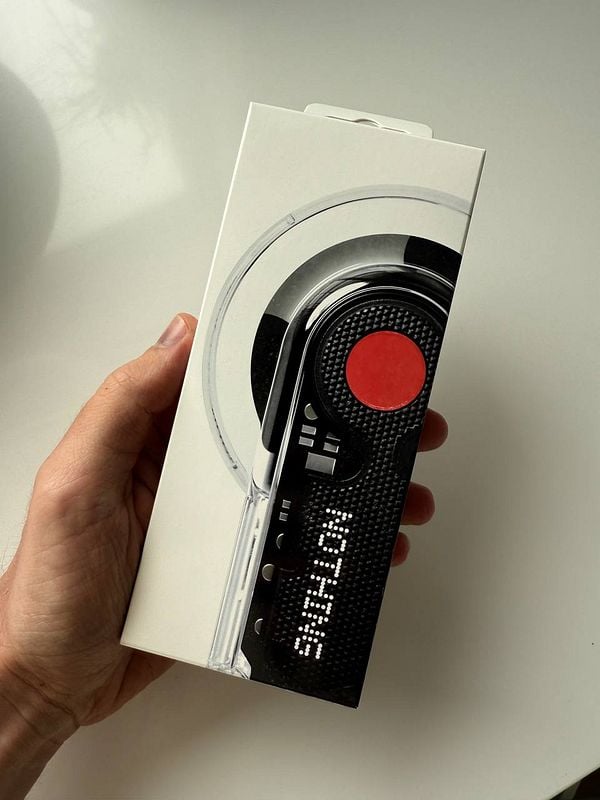 A hand holds a sleek, modern packaging for earpods from the brand Nothing.