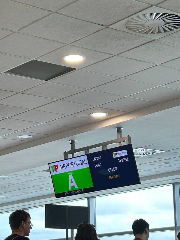 The image displays a flight information board at an airport showing details for a flight to Lisbon.