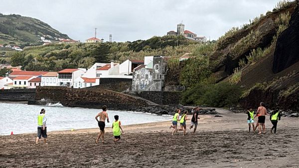 A group of children and adults are playing ultimate frisbee on a beach.