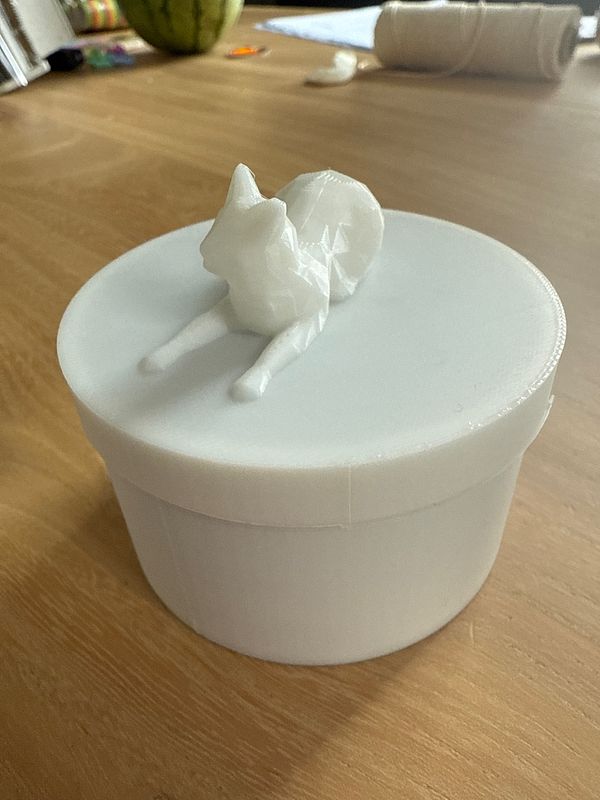 A 3D printed cat food holder with a cat figurine on top is placed on a wooden table.