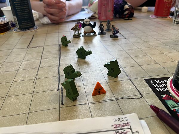 A tabletop gaming scene featuring miniatures and game pieces on a grid map.