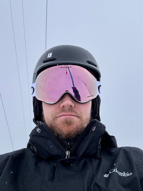 A skier wearing a helmet and goggles poses against a snowy backdrop.