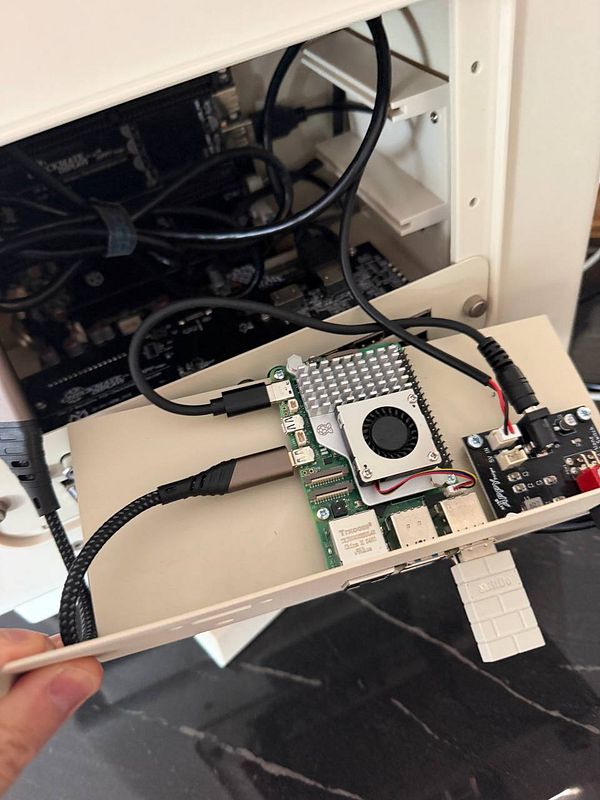 Open retro PC case with Raspberry Pi 5 mounted on a panel being held outside, showing power and data connections.