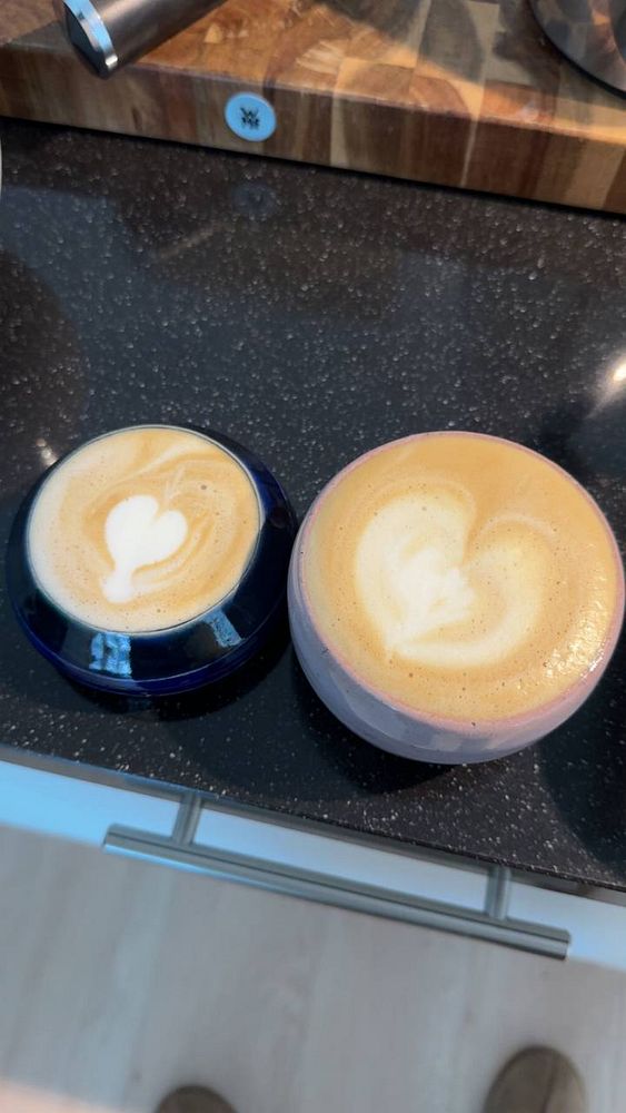 A white ceramic coffee cup filled with coffee is placed on a wooden surface next to a beige knit fabric.