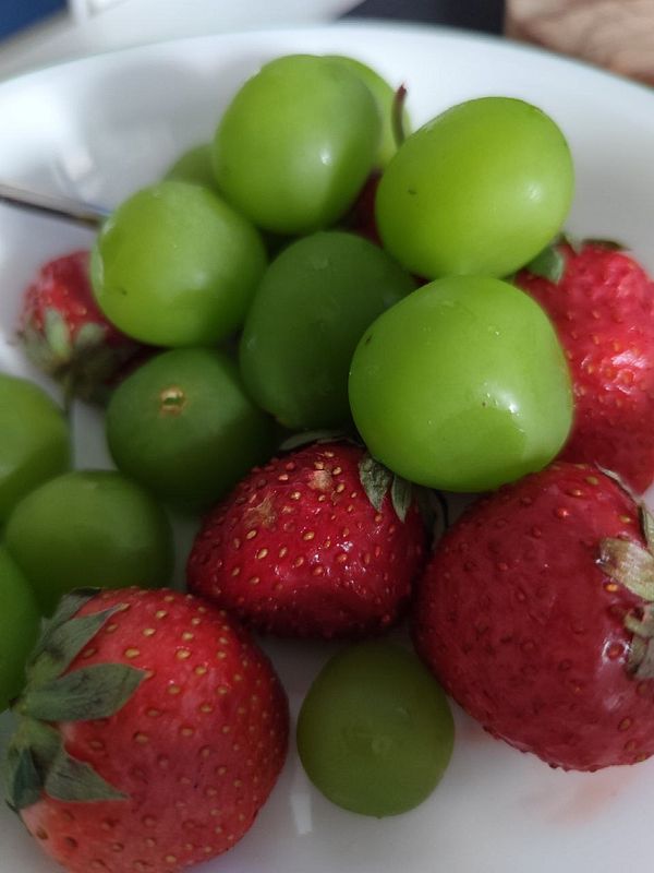 A close-up view of a bowl filled with fresh strawberries and green grapes.