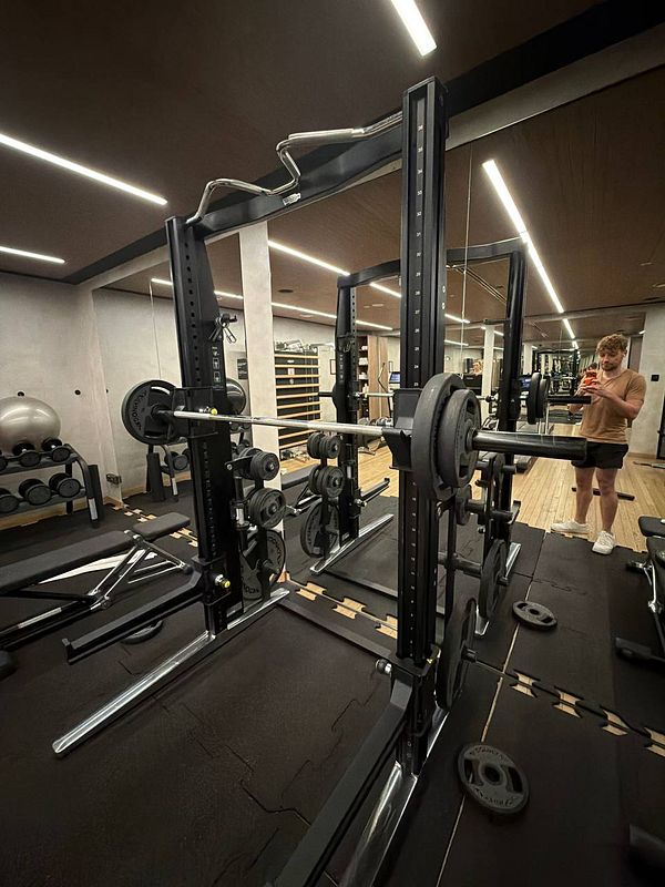 A gym scene with weight lifting equipment and a man taking a mirror selfie.