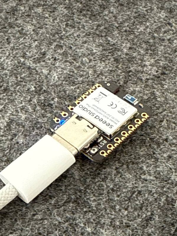 A close-up view of a Seed Studio XIAO nRF52840 microcontroller connected via a USB cable.