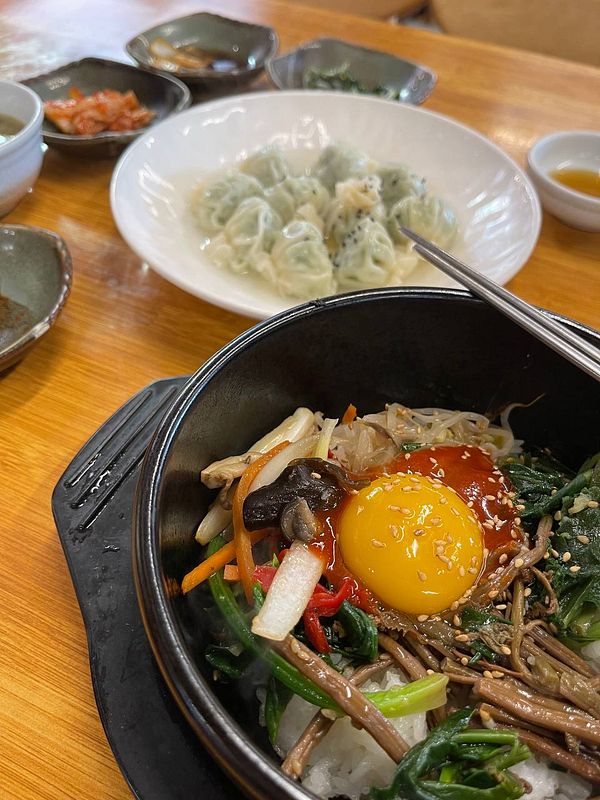 A vibrant bowl of bibimbap accompanied by dumplings and various side dishes.