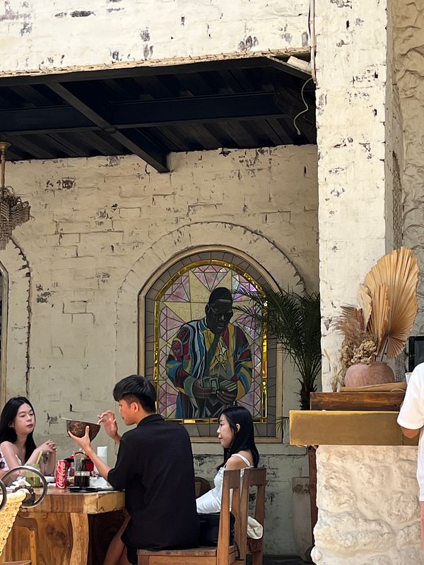 A vibrant dining scene featuring a stained glass window and patrons enjoying their meal.