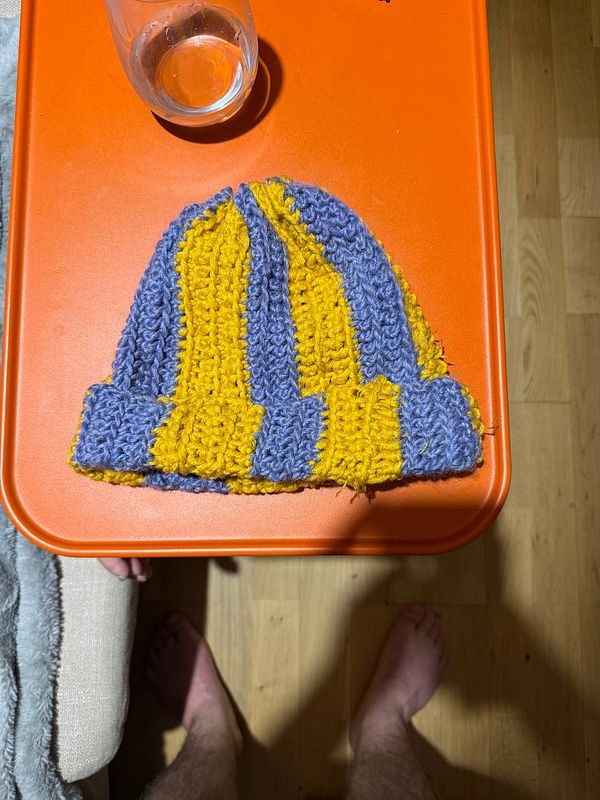 A handmade crochet beanie in blue and yellow sits on an orange table.