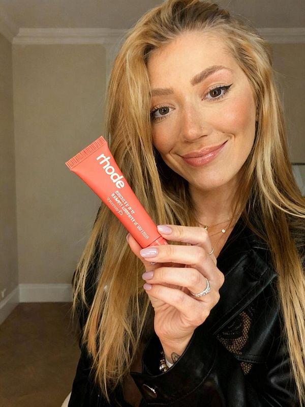 A woman holds a tube of skincare product while smiling at the camera.