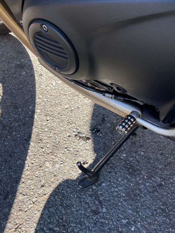 A motorcycle is parked on a gravel surface, showing an oil leak beneath it.