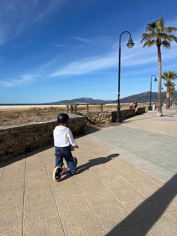 A child rides a balance bike along a scenic promenade by the beach.