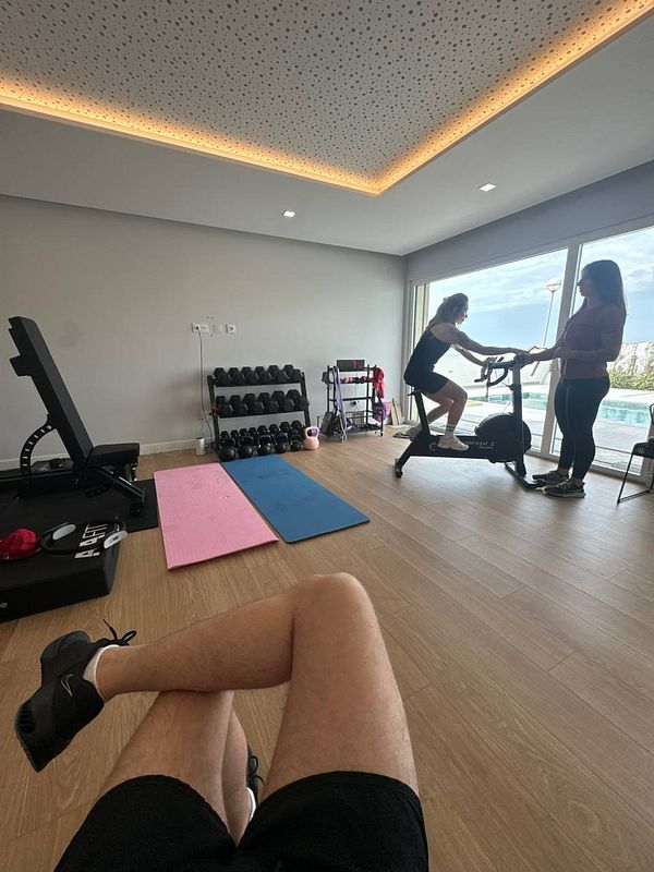 A home gym setting with a personal trainer assisting a client on an exercise bike.