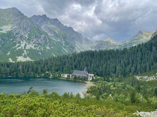 A scenic view of a mountain lake surrounded by lush forests and towering peaks under a cloudy sky.