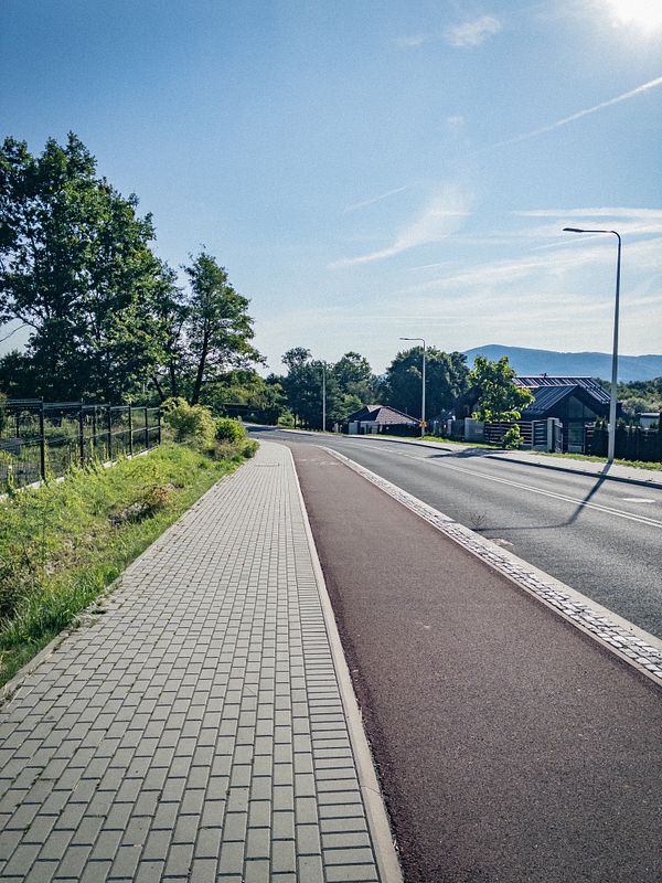 A scenic morning landscape alongside a canal with a walking path, trees, and urban buildings in the background.
