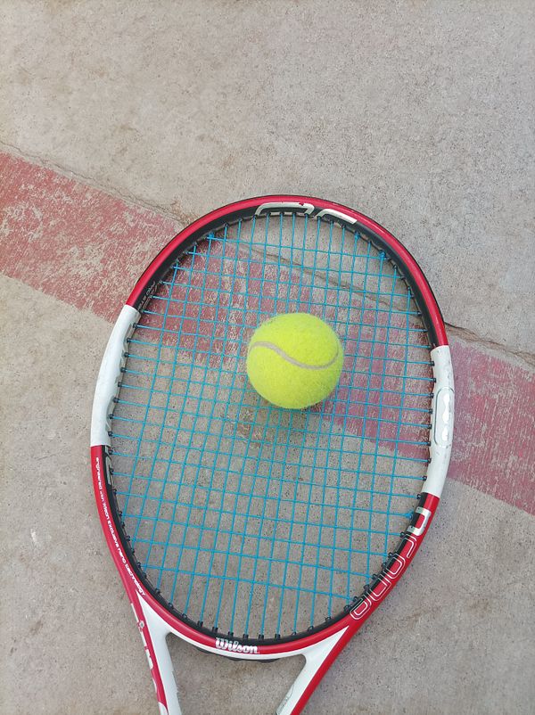 A tennis racket with a bright yellow tennis ball resting on its strings.