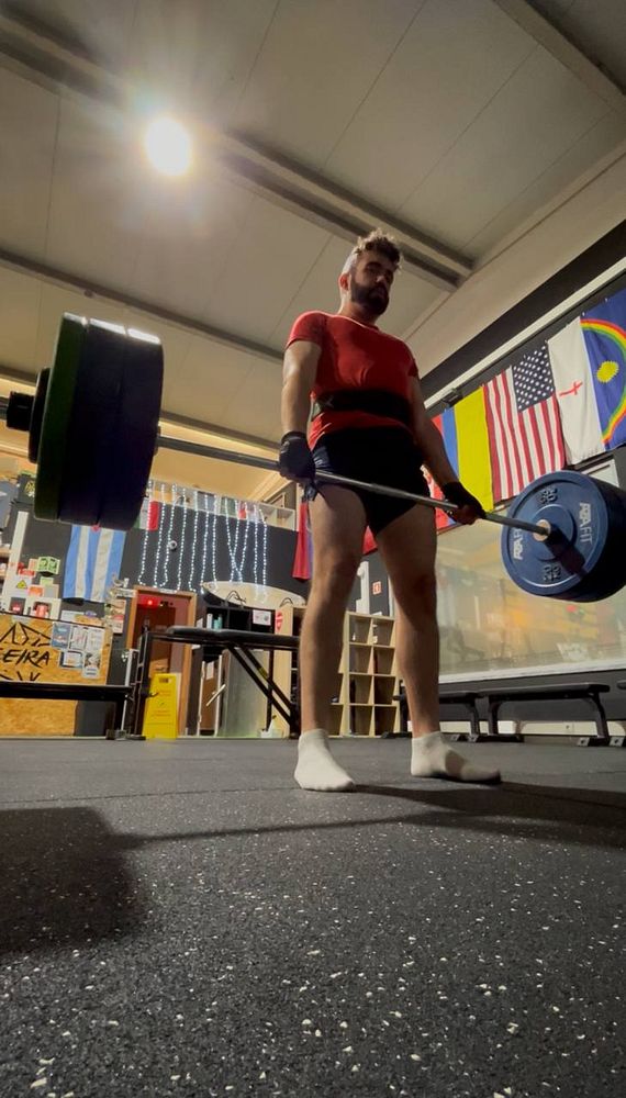 A person is preparing to deadlift a barbell loaded with weights in a gym setting.