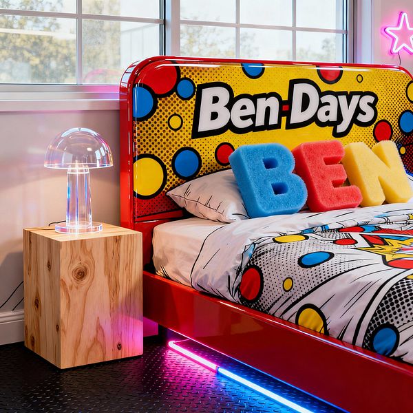A kids' bedroom styled like a comic book, featuring a glossy red bed with a large headboard reading 'Ben-Days' over yellow Ben-Day dots and red and blue circles. The bed has white cotton sheets printed with cartoon graphics and three plush letters spelling BEN. A clear acrylic mushroom lamp sits on a knotty pine cube nightstand. Neon pink and blue light strips glow under the bed, with a pink star neon on the wall, black coin rubber flooring, and a wide white-framed window.