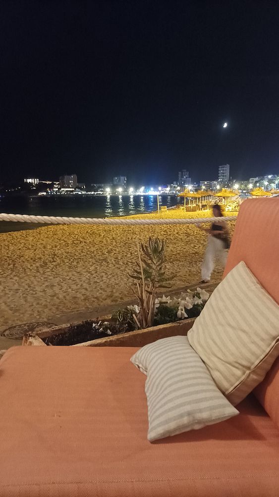 A cozy beachside scene at night featuring a lounge chair and a view of the illuminated shoreline.